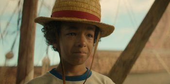 Movie still from “One Piece” (2023), directed by Marc Jobst – A young boy wearing a straw hat and looking at the camera; Close Up shot, Low angle