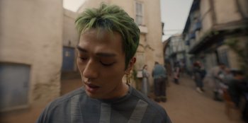 Movie still from “One Piece” (2023), directed by Marc Jobst – A young man with green hair is standing in a street; Close Up shot, Low angle