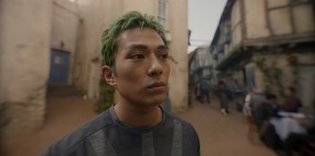 Movie still from “One Piece” (2023), directed by Marc Jobst – A man with green hair standing on a sidewalk; Close Up shot, Low angle
