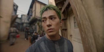 Movie still from “One Piece” (2023), directed by Marc Jobst – A man with green hair is standing in a street; Close Up shot, Low angle
