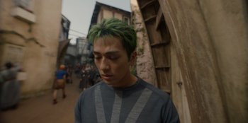 Movie still from “One Piece” (2023), directed by Marc Jobst – A man with green hair is walking down the street; Close Up shot, Low angle