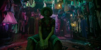 Movie still from “One Piece” (2023), directed by Marc Jobst – A man sitting on top of a chair in front of a bunch of clothes; Medium shot, Low angle