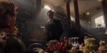 Movie still from “One Piece” (2023), directed by Marc Jobst – A man in a suit standing in front of a table; Medium shot, Low angle