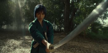 Movie still from “One Piece” (2023), directed by Marc Jobst – A person holding a sword in a forest; Medium shot, Low angle