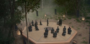 Movie still from “One Piece” (2023), directed by Marc Jobst – A group of people sitting on top of an octagon shaped platform; Extreme Wide shot, High angle