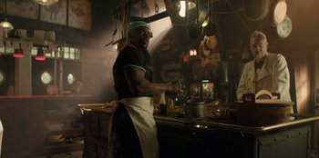 Movie still from “One Piece” (2023), directed by Marc Jobst – A man standing in a kitchen preparing food; Medium shot, Low angle