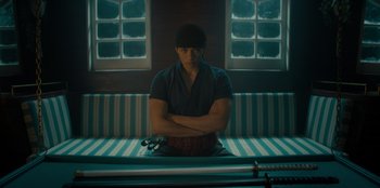 Movie still from “One Piece” (2023), directed by Marc Jobst – A man sitting on top of a bench with his arms crossed; Medium shot, Low angle