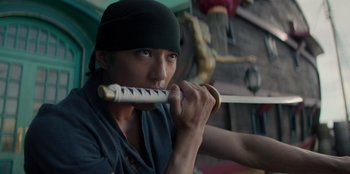 Movie still from “One Piece” (2023), directed by Marc Jobst – A man holding a sword in his mouth; Close Up shot, Low angle