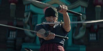 Movie still from “One Piece” (2023), directed by Marc Jobst – A man holding a pair of swords while wearing a blindfold; Medium shot, Low angle