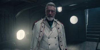 Movie still from “One Piece” (2023), directed by Marc Jobst – An older man with a beard wearing a white jacket; Medium shot, Low angle
