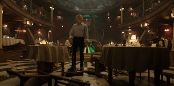 Movie still from “One Piece” (2023), directed by Marc Jobst – A man standing in a room that has tables , chairs , and tables in it; Wide shot, Low angle