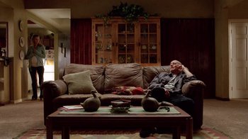 Movie still from “Breaking Bad” (2008), created by Vince Gilligan – A man sitting on top of a brown couch next to a coffee table; Wide shot, Low angle
