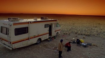 Two people standing in front of an rv in the desert at sunset
