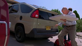 Movie still from “Breaking Bad” (2008), created by Vince Gilligan – A man holding an object in front of a car; Wide shot, Low angle