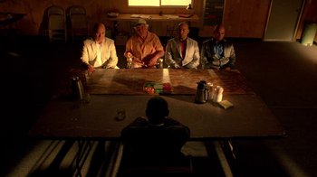Movie still from “Breaking Bad” (2008), created by Vince Gilligan – A group of men sitting at a table in a room; Wide shot, High angle