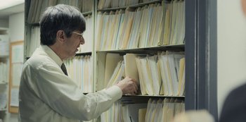 Movie still from “Paddleton” (2019), directed by Alex Lehmann – A man in a white shirt is looking at papers; Medium shot, Over the shoulder angle