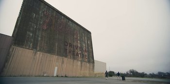 Movie still from “Paddleton” (2019), directed by Alex Lehmann – People are walking on the street in front of an old theater; Extreme Wide shot, Low angle