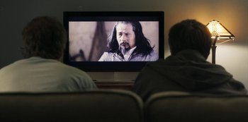 Movie still from “Paddleton” (2019), directed by Alex Lehmann – Two people sitting in front of a television; Medium shot, Over the shoulder angle