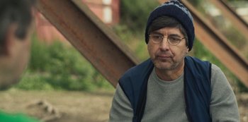 Movie still from “Paddleton” (2019), directed by Alex Lehmann – A man wearing glasses and a hat sitting on the ground; Close Up shot, Over the shoulder angle