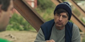 Movie still from “Paddleton” (2019), directed by Alex Lehmann – A man wearing glasses and a hat sitting on the ground; Close Up shot, Over the shoulder angle
