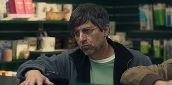 Movie still from “Paddleton” (2019), directed by Alex Lehmann – A man in a green shirt is sitting at a table in a store; Close Up shot, Over the shoulder angle