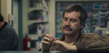 Movie still from “Paddleton” (2019), directed by Alex Lehmann – A man sitting at a table in a room; Close Up shot, Over the shoulder angle