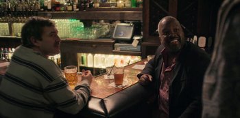 Movie still from “Paddleton” (2019), directed by Alex Lehmann – A man sitting at a bar with two glasses of beer in front of him; Medium shot, Over the shoulder angle