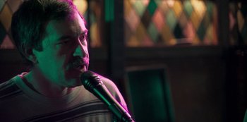 Movie still from “Paddleton” (2019), directed by Alex Lehmann – A man holding a microphone while standing in a room; Close Up shot, Over the shoulder angle