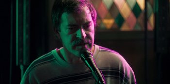 Movie still from “Paddleton” (2019), directed by Alex Lehmann – A man with a mustache is holding a microphone in front of him; Close Up shot, Low angle