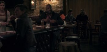 Movie still from “Paddleton” (2019), directed by Alex Lehmann – A man sitting at a table in front of a brick wall; Wide shot, Over the shoulder angle