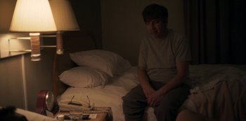 Movie still from “Paddleton” (2019), directed by Alex Lehmann – A man sitting on top of a bed next to a lamp; Medium shot, High angle