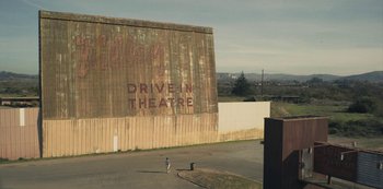 Movie still from “Paddleton” (2019), directed by Alex Lehmann – An old drive - in theater with a man walking down the street; Extreme Wide shot, Low angle