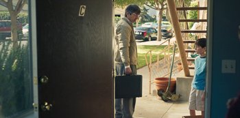 Movie still from “Paddleton” (2019), directed by Alex Lehmann – A man holding a briefcase while standing in a doorway; Wide shot, Over the shoulder angle