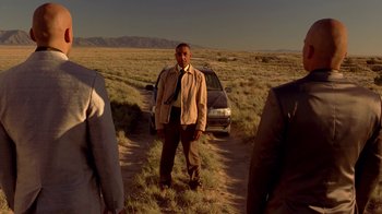 Movie still from “Breaking Bad” (2008), created by Vince Gilligan – A man standing next to a car on a dirt road; Medium shot, Low angle