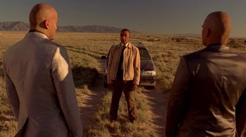 Movie still from “Breaking Bad” (2008), created by Vince Gilligan – A man standing next to a car on a dirt road; Wide shot, Over the shoulder angle