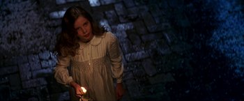Movie still from “Peter Pan” (2003), directed by P.J. Hogan – A young girl holding a lit candle in a dark place; Medium shot, High angle
