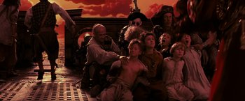 Movie still from “Peter Pan” (2003), directed by P.J. Hogan – A group of people sitting on the ground with a sky in the background; Wide shot, Low angle