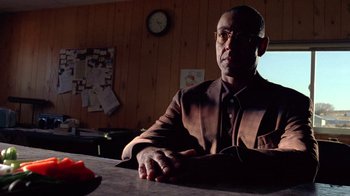 Movie still from “Breaking Bad” (2008), created by Vince Gilligan – A man sitting at a table in front of a clock; Medium shot, Low angle