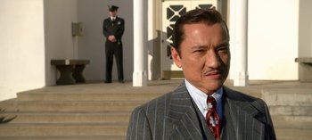 Movie still from “Ratched” (2020), created by Evan Romansky – A man in a suit and tie standing in front of a building; Close Up shot, Low angle