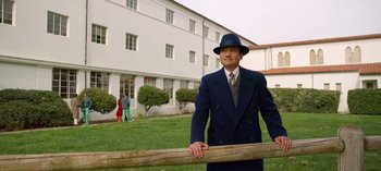 Movie still from “Ratched” (2020), created by Evan Romansky – A man in a suit and hat leaning on a wooden fence; Wide shot, Low angle