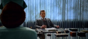 Movie still from “Ratched” (2020), created by Evan Romansky – A man sitting at a table in front of a curtain; Medium shot, Over the shoulder angle