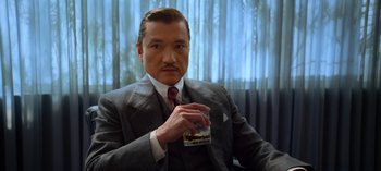 Movie still from “Ratched” (2020), created by Evan Romansky – A man in a suit and tie holding a glass; Close Up shot, Low angle
