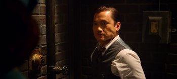 Movie still from “Ratched” (2020), created by Evan Romansky – A man in a vest and tie standing in front of a brick wall; Medium shot, Low angle