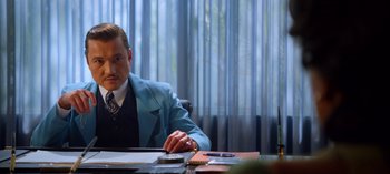 Movie still from “Ratched” (2020), created by Evan Romansky – A man sitting at a desk in a suit and tie; Medium shot, Over the shoulder angle