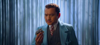 Movie still from “Ratched” (2020), created by Evan Romansky – A man in a blue suit holding a doughnut; Close Up shot, Over the shoulder angle