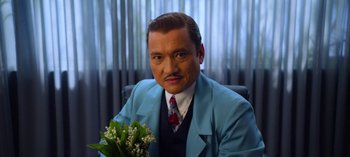 Movie still from “Ratched” (2020), created by Evan Romansky – A man in a blue suit holding a bouquet of flowers; Close Up shot, Low angle