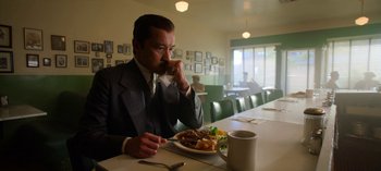 Movie still from “Ratched” (2020), created by Evan Romansky – A man sitting at a table with a plate of food in front of him; Medium shot, Low angle