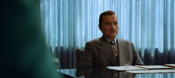 Movie still from “Ratched” (2020), created by Evan Romansky – A man sitting at a table in front of a curtain; Medium shot, Over the shoulder angle