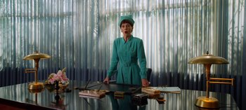 Movie still from “Ratched” (2020), created by Evan Romansky – An older woman in a turquoise suit stands at a desk; Medium shot, Low angle