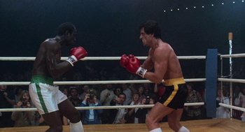 Movie still from “Rocky III” (1982), directed by Sylvester Stallone – Two boxers in a boxing ring during a match; Wide shot, Low angle